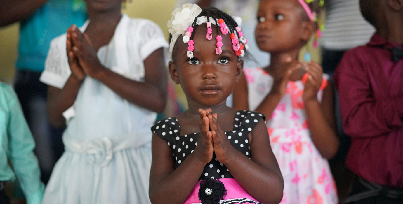 A Haitian girl holds her hands in prayer.