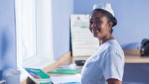 A health worker stands in her workspace, smiling. 